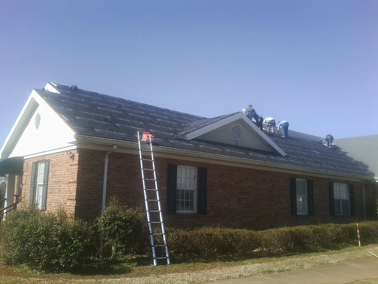 Crew tearing shingles off a brick ranch roof with a ladder set — Metal Roof Repair work by our crew in Jay