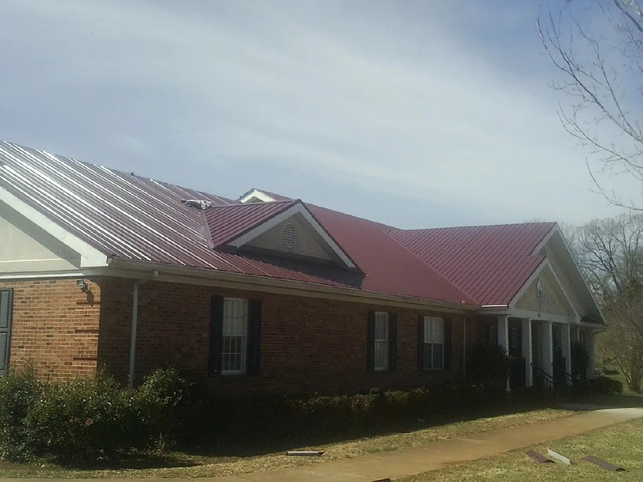 Red metal roof with gabled entries on a long brick building, from a Hail Damage Roof Repair job in Jay