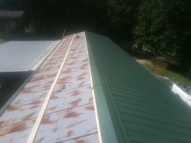 Old rusted panels beside newly installed green metal roofing — Wind Damage Roof Repair by Roofing Brothers in Jay