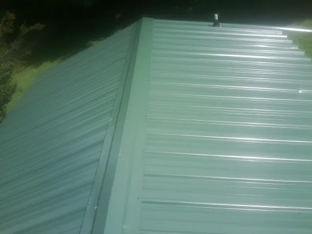 New green metal panels meeting at the ridge of a roof — Flat Roof Repair work by our crew in Jay