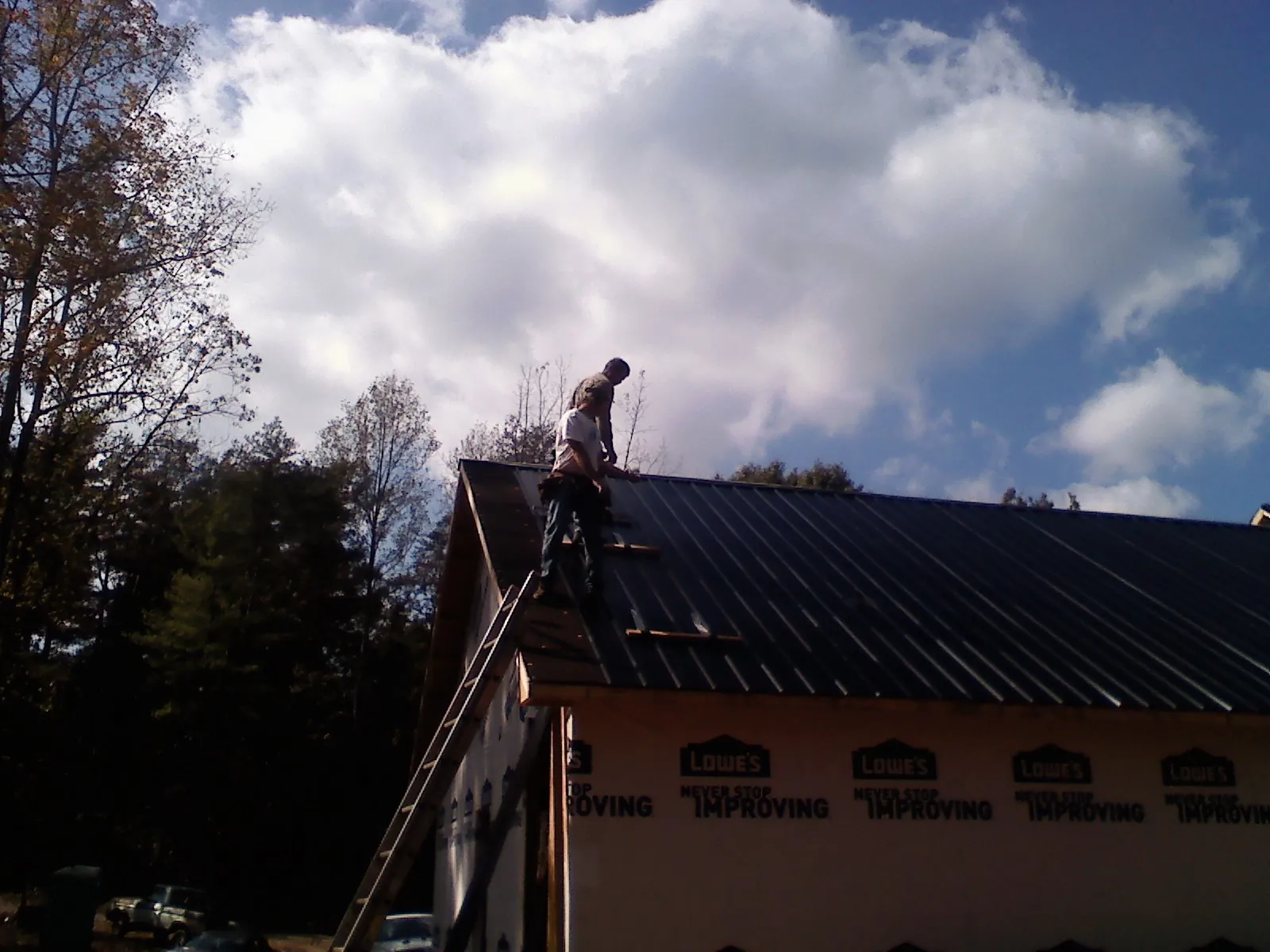 Roofer fastening dark metal panels high against a cloudy sky, from a Roof Inspection job in Jay